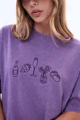 Remera de algodón con efecto lavado, color violeta, de corte oversize y manga corta. Presenta un estampado lineal en el pecho con dibujos de una botella, una fresa, una copa, un florero y una fruta.