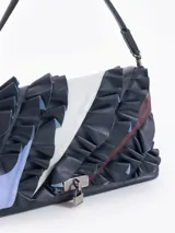 Cartera de hombro negra confeccionada en cuero vacuno, con diseño de solapa frontal decorada con volados de cuero y cierre metálico tipo candado.