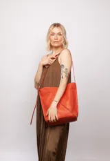 Bolso tipo bucket de cuero color marrón con costuras a la vista, doble bolsillo interior (uno con cierre) y correa regulable.