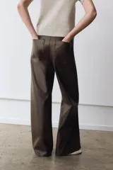 Pantalón de tiro alto confeccionado en tejido efecto piel, con diseño de pierna ancha y costuras marcadas en el delantero. Presenta cintura con trabillas, cierre frontal con cremallera, botón y gancho metálico, y bolsillos de plastrón en la espalda.