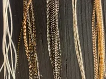 Mix de plumas para cabello, incluyendo plumas largas con patrón moteado/rayado en tonos marrones y grises, y plumas finas lisas en tonos blanco y naranja.