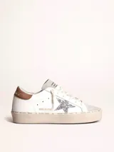 Zapatillas urbanas Golden Goose modelo Hi Star, de cuero blanco con detalles en gris y marrón. Presentan una estrella plateada con glitter en el lateral y suela de goma con inscripciones.