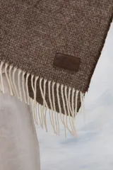 Ruana de lana 100% sin teñir en color tostado, con diseño de punto acanalado y terminación de flecos en el ruedo.