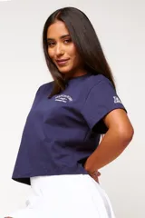 Remera blanca de algodón con corte crop, mangas cortas y estampado frontal con texto y logo en color gris.