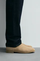 Bota estilo Chelsea de piel con acabado serraje color beige, con elásticos laterales para facilitar el calce, horma redonda y suela a tono con ligero tacón.