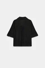 Camisa negra de textura arrugada, con cuello solapa, escote en V y cierre frontal de botones. Cuenta con mangas cortas terminadas en vuelta con trabilla y botón.