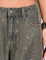 Jean de corte wide leg confeccionado en algodón con aplicación integral de strass. Presenta un diseño de tiro medio, cierre frontal con botón y bolsillos laterales.