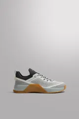 Zapatilla deportiva de entrenamiento con parte superior de tejido de punto transpirable en tonos grises. Presenta refuerzos Shield Protect Max en puntera y talón, cierre mediante cordones, tirador posterior y entresuela con tecnología Stabi-pro sobre una suela de goma color caramelo.