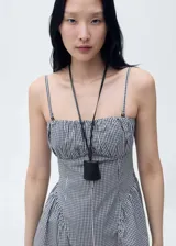 Vestido midi de corte evasé con estampado de cuadros vichy en blanco y negro. Presenta un diseño sin mangas con tirantes finos ajustables, escote recto con detalle fruncido y cierre de cremallera lateral.