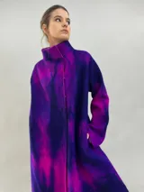Tapado de lana merino afieltrada con diseño artesanal teñido en tonos violeta y fucsia. Presenta cuello elevado, cierre frontal con broches ocultos, bolsillos laterales y un corte ligeramente más largo en la parte trasera.