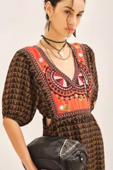 Vestido largo de viscosa con estampado geométrico en tonos marrones y detalle de bordado colorido en el escote en V. Presenta mangas cortas con frunces y puños elásticos, cintura elástica y cierre lateral invisible.