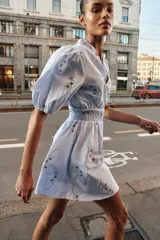 Vestido corto de color celeste con estampado floral, cuello redondo con volante y escote en pico. Presenta mangas cortas abullonadas con puños elásticos y cintura con nido de abeja elástico.