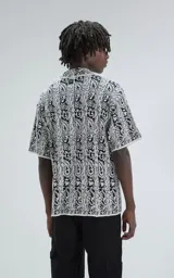 Camisa de manga corta, tejida de punto abierto (símil crochet), color blanco y negro con estampado paisley. Tiene cuello tipo solapa y calce oversize.