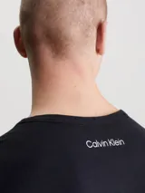 Conjunto de pijama Calvin Klein 1996, compuesto por una remera negra de algodón con cuello redondo, manga corta y logo estampado en el pecho, y un short de algodón tejido con estampado floral en blanco y negro, bolsillos laterales y cintura elástica con logo distintivo de la marca. Incluye bolsa de CK a juego.