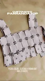 Top tipo armadura o corsé, confeccionado con tiras superpuestas de material blanco perforado (tipo puntillado) unidas entre sí mediante argollas metálicas. Presenta un diseño personalizable en color, textura y forma (Halter, Cuello cuadrado o Cuello en V).