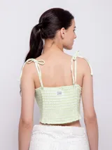 Top corto con escote recto y tirantes finos ajustables mediante nudo en los hombros. Presenta un estampado floral sobre fondo oscuro, con flores rosadas y hojas turquesas.