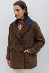 Tapado de paño color marrón con diseño de doble abotonadura, solapas amplias y cuello en contraste color azul marino. Presenta silueta oversize con hombros caídos, mangas con ajuste en puños y bolsillos laterales con ribete en contraste.