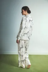 Pijama de dos piezas compuesto por camisa de manga larga con botones y pantalón recto, confeccionado en tela satinada color crema con estampado de cebras en negro.