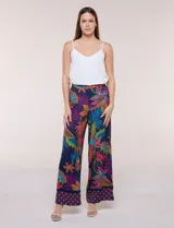 Pantalón pull on largo de caída fluida, cintura alta con pretina trasera elastizada, pierna de corte ancho tipo palazzo y detalle de guarda geométrica sobre el ruedo inferior, con estampado floral multicolor sobre base azul.