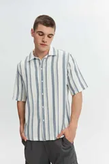 Camisa de manga corta oversize en tejido rústico, con diseño de rayas verticales celestes y blancas, cuello clásico y cierre frontal de botones.