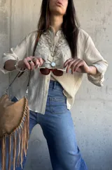 Camisa beige de manga larga con diseño bordado en el pecho, cuello camisero y cierre frontal de botones.
