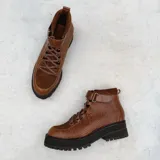 Botas negras de caña baja con textura simil reptil, cordones, suela flatform dentada y tira con hebilla en el tobillo.