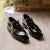 Zapato mocasín de cuero vacuno color negro charol, con cordones, punta redonda y taco de madera foliado en cuero de 2,5 cm.