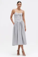 Vestido midi gris con diseño de raya diplomática, tirantes finos, corpiño tipo corsé estructurado con apliques de cristales y pedrería, y falda amplia con bolsillos.