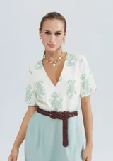 Blusa color beige con estampado de hojas color verde agua, escote en V y mangas cortas.