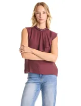 Blusa sin mangas color blanco, confeccionada en crepe con acabado satinado. Presenta un cuello alto decorado con mostacillas y una sobrecapa drapeada en el frente. La espalda cuenta con una abertura tipo gota y cierre de botón.