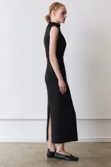 Vestido midi de color negro, con cuello subido y diseño sin mangas. Presenta un detalle de drapeado lateral en la parte delantera y cierre de cremallera oculta en la espalda.