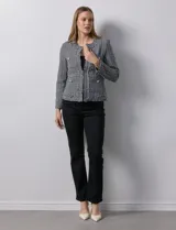 Chaqueta Nanette de tejido tweed color beige, con cuello a la base, abertura central y bolsillos delanteros. Tiene apliques de botones perlados en los puños, terminación desflecada y forro interno.