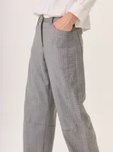 Pantalon de corte recto y tiro medio, confeccionado en tejido de lana con sutiles rayas verticales. Presenta bolsillos traseros aplicados, costuras reforzadas en las rodillas y ruedo con dobladillo.