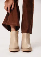 Botín de cuero color beige con textura reptil, elástico lateral y cierre interno. Tiene plataforma delantera y taco de madera.