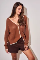 Cardigan de punto color marrón, de corte holgado y manga larga, con escote en V y cierre frontal de botones. Presenta detalles de terminación festoneada en color blanco en los bordes.