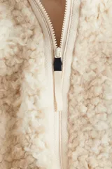 Campera de sherpa suave con cuello elevado acanalado y cierre frontal. Modelo con bolsillos laterales discretos, bolsillo interior y cordones para ajustar en el bajo.