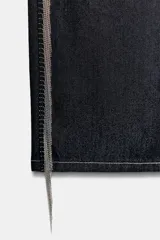 Jeans de tiro bajo y corte recto en denim color azul oscuro. Presenta cinco bolsillos, trabillas para cinturón y cierre frontal con cremallera y botón metálico. Destaca por la aplicación de flecos brillantes en los laterales de ambas piernas.