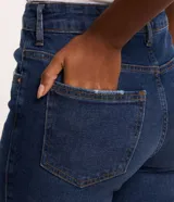Pantalón de jean skinny azul oscuro con trabillas en la cintura, cierre tradicional por botón y cremallera, bolsillos delanteros y traseros deshilachados y costuras verticales.