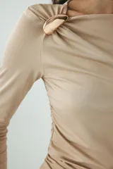 Top entallado de manga larga color beige en punto suave, con escote asimétrico fruncido, detalle metálico en el hombro y frunces laterales con efecto drapeado.