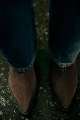 Botín de mujer color marrón oscuro, de serraje con acabado en punta y cierre mediante cremallera. Tiene un tacón estilo cowboy.