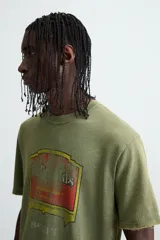 Camiseta de punto de algodón con corte relaxed fit, cuello redondo y manga corta. Color verde oliva con efecto lavado y estampado frontal con diseño gráfico en tonos rojo y amarillo.