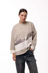 Sweater de punto con diseño de bloques de color en diagonal, combinando negro, beige y una franja central con textura metalizada. Presenta cuello redondo, mangas largas con puños en contraste y un corte holgado.