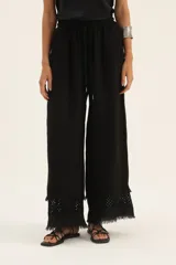Pantalón negro de corte palazzo con cintura elastizada y cordón ajustable. Presenta detalle de bordado broderie en el ruedo.