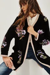 Cardigan negro de punto con bordados florales y aplicaciones de lentejuelas. Presenta terminaciones en tejido acanalado de color beige en los puños, el ruedo y a lo largo de la apertura frontal.