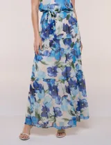 Vestido maxi largo de gasa estampada con diseño floral en tonos azules y verdes sobre base clara, de escote halter y sin mangas. Cuenta con cintura elastizada, lazo de ajuste y falda estructurada en paneles escalonados con forro interno.