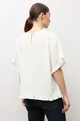Blusa crudo con textura plumetti, escote redondo y mangas cortas terminadas en delicados volados.