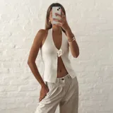 Top halter blanco de tejido de punto, con escote en V pronunciado y detalle de aplicación floral en el centro.