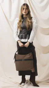 Cartera tipo hobo de tamaño grande en color beige, con detalles en negro. Presenta una franja horizontal negra con el logo de la marca, asa corta de hombro y correa larga desmontable. Incluye bolsillo frontal con cierre oculto y bolsillo trasero.