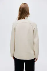Buzo de punto oversized con cuello tortuga acanalado y abertura en la nuca. Presenta mangas raglán con costuras decorativas y terminaciones acanaladas en puños y bajo.
