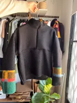 Buzo de cuello alto confeccionado en tejido polar texturizado, con diseño combinado que presenta un sector superior y puños estampados a cuadros en tonos verdes, amarillos, naranjas, celestes y negros, y la parte inferior y mangas en color negro liso.